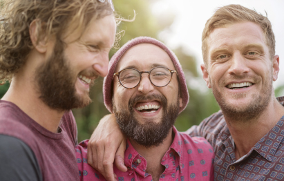Drei lächelnde Männer, die eng beieinanderstehen und Spaß haben.