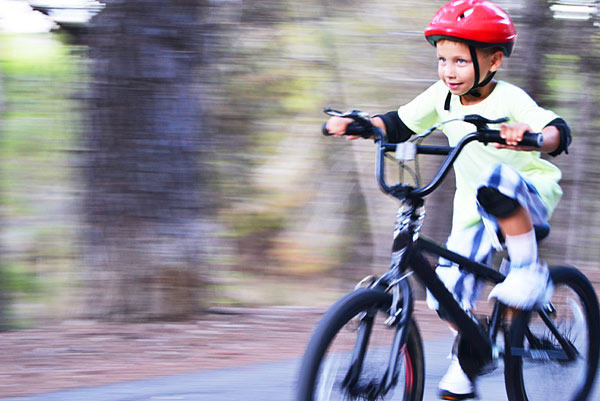 Ein Junge in einem roten Helm fährt schnell auf einem Fahrrad.